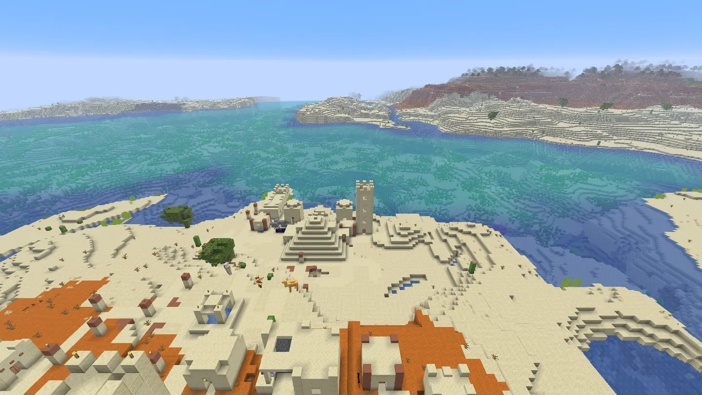 Sandstone desert temple beside village houses, orange badlands and blue coastal water. In-game screenshot, Java 26.3.