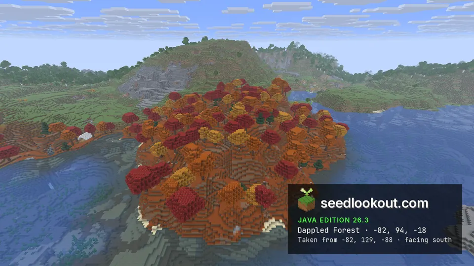 Hill covered in red, orange and yellow trees sloping down to a blue lake, green hills behind