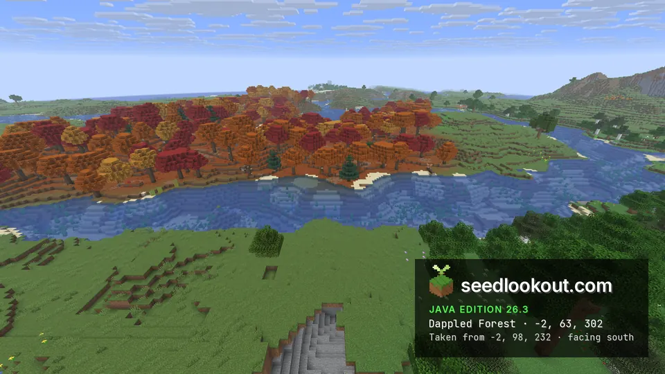 Band of red and orange trees across a winding river, green grass in the foreground